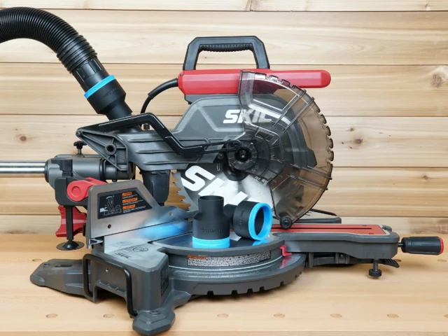 Two black ToolCurve 2-1/2 inch hose adapters with blue rings resting on a SKIL 10 inch miter saw table, one attached to a hose