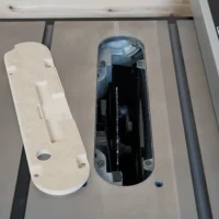 Zero clearance insert for Delta table saw displayed next to original insert, showing white MDF construction with mounting holes and blade slot cutouts