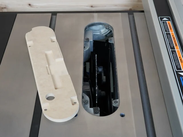 Zero clearance insert for Delta table saw displayed next to original insert, showing white MDF construction with mounting holes and blade slot cutouts
