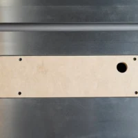 Light MDF zero clearance insert with rounded ends, four mounting holes, and one blade slot, positioned on a gray metal table saw surface