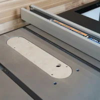 Light wood zero clearance insert with mounting holes installed in Delta Contractor table saw blade opening, white fence visible above