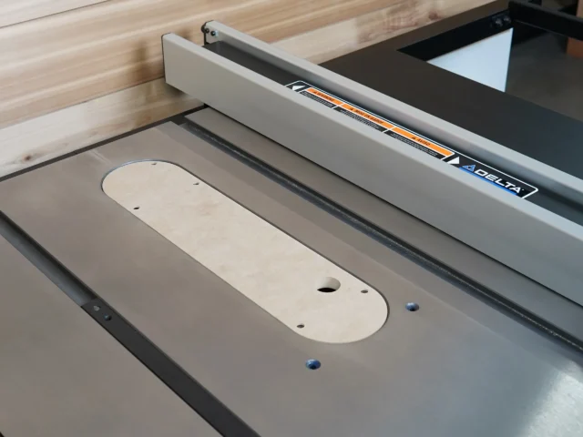 Light wood zero clearance insert with mounting holes installed in Delta Contractor table saw blade opening, white fence visible above