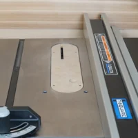 Cream-colored zero clearance insert installed in Delta Contractor table saw, with slot for blade visible and mounting holes exposed