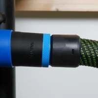 Black 36mm hose adapter with blue ring joining a Delta table saw dust port to a green braided vac hose