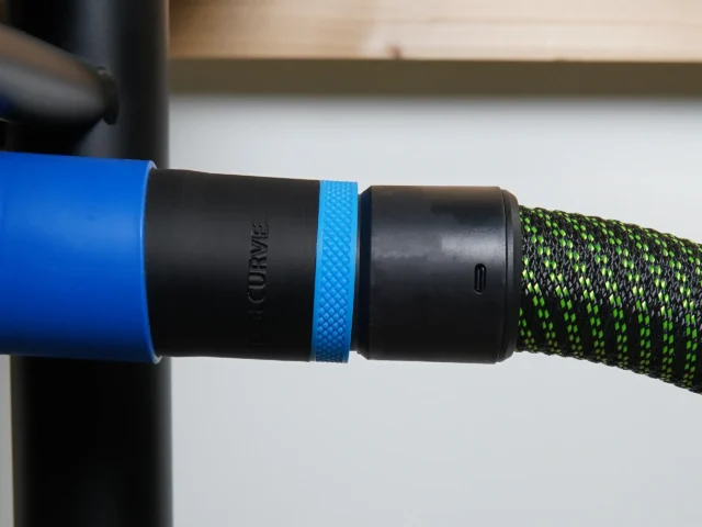 Black 36mm hose adapter with blue ring joining a Delta table saw dust port to a green braided vac hose
