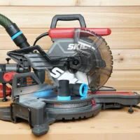Black 36mm hose adapters with blue rings resting on a SKIL 10-inch miter saw table, hose connected above