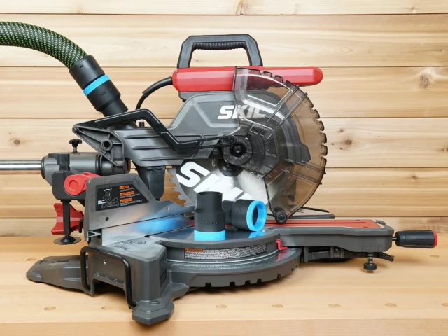 Black 36mm hose adapters with blue rings resting on a SKIL 10-inch miter saw table, hose connected above