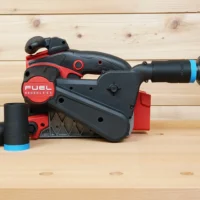 Black 1-1/4" hose adapter with blue band fitted to a Milwaukee M18 belt sander dust port, spare adapter beside it
