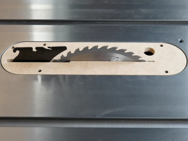 Light wood zero clearance insert with curved edges and saw blade cutout, mounted on metal table saw top