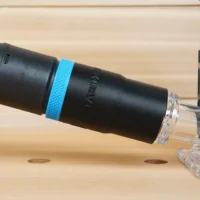 Black hose adapter with blue grip band attached to Metabo HTP cordless trim router dust port, showing clear threaded connector end