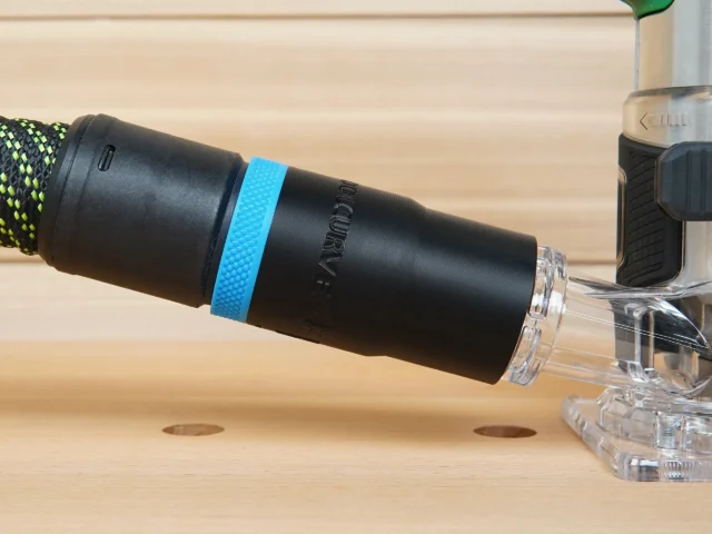Black hose adapter with blue grip band attached to Metabo HTP cordless trim router dust port, showing clear threaded connector end