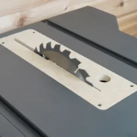 Light MDF zero clearance insert with saw blade slot and mounting holes, laid on gray table saw top
