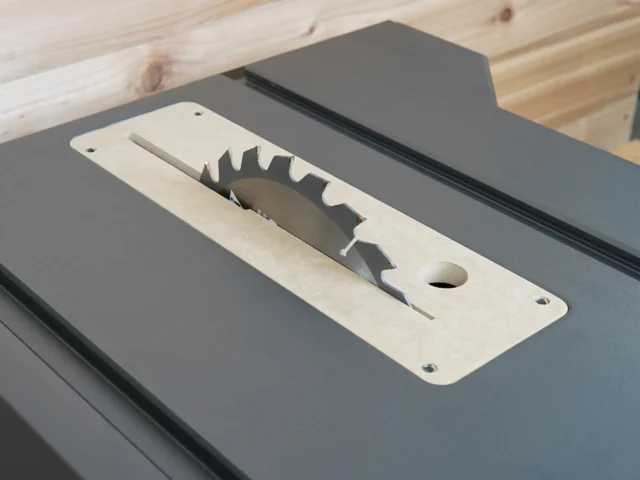 Light MDF zero clearance insert with saw blade slot and mounting holes, laid on gray table saw top