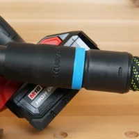 Black hose adapter with blue band installed on Milwaukee M18 circular saw dust port, connected to braided hose