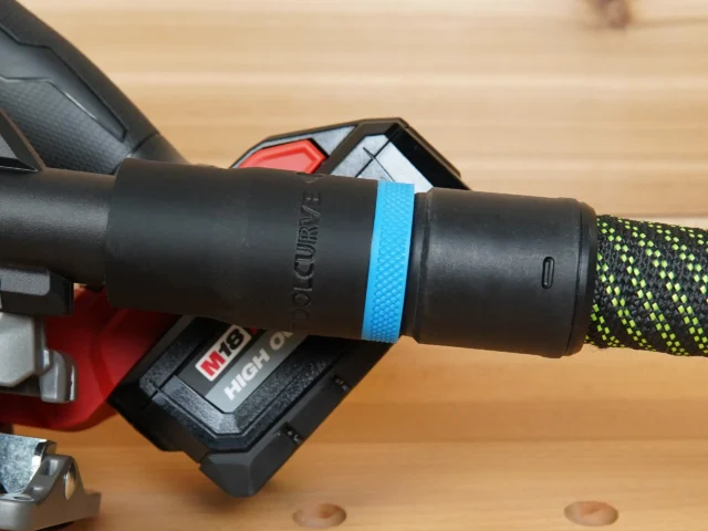 Black hose adapter with blue band installed on Milwaukee M18 circular saw dust port, connected to braided hose