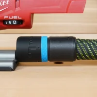 Black hose adapter with blue band attached to Milwaukee M18 Fuel jig saw dust port, with braided hose connected