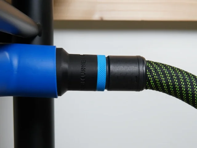 Black hose adapter with blue band attached to blue Delta table saw dust port, connected to black and green braided hose