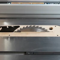 Light wood zero clearance insert with curved edges and slots for mounting, installed on gray Delta contractor table saw