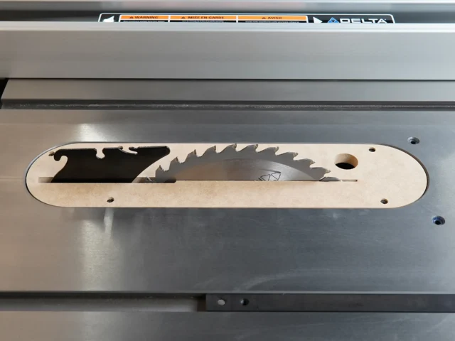 Light wood zero clearance insert with curved edges and slots for mounting, installed on gray Delta contractor table saw