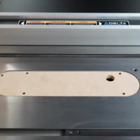 Cream-colored MDF zero clearance insert installed on a Delta contractor table saw, showing mounting holes and center blade opening.