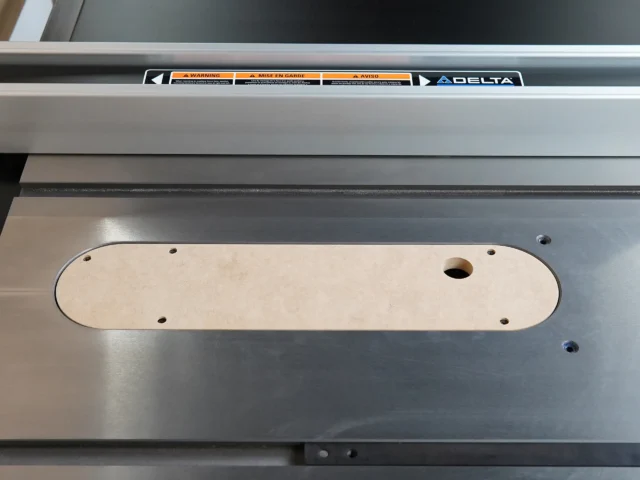 Cream-colored MDF zero clearance insert installed on a Delta contractor table saw, showing mounting holes and center blade opening.