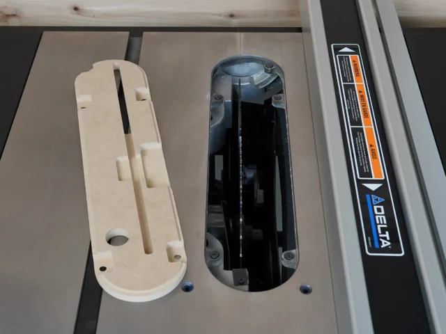 Cream-colored MDF zero clearance insert for Delta table saw alongside black factory insert, showing slots and mounting holes