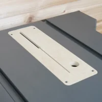 Cream-colored zero clearance insert with centered slot and mounting holes, positioned on gray SKIL table saw