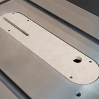 Light-colored MDF zero clearance insert for Ridgid R4560 table saw, positioned in the saw's slot with rectangular blade opening and mounting holes visible