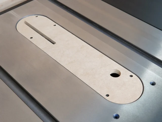 Light-colored MDF zero clearance insert for Ridgid R4560 table saw, positioned in the saw's slot with rectangular blade opening and mounting holes visible