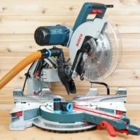 Bosch 12 in. glide miter saw with black 1-1/4 in. hose adapter joining an orange vacuum hose to the dust port