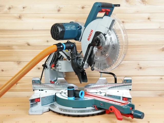 Bosch 12 in. glide miter saw with black 1-1/4 in. hose adapter joining an orange vacuum hose to the dust port