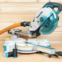 Black 1-1/4" hose adapter installed on a Makita LS miter saw dust port with orange hose, spare adapter alongside