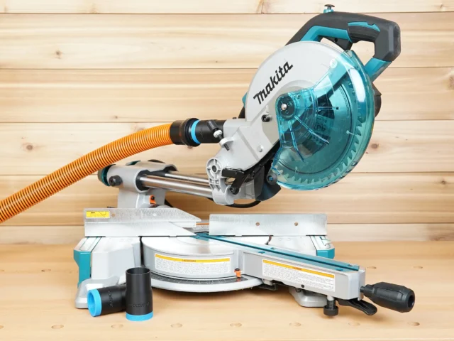 Black 1-1/4" hose adapter installed on a Makita LS miter saw dust port with orange hose, spare adapter alongside