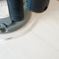 Clear acrylic router base plate attached to Bosch 1617 router, showing 8-inch diameter with mounting hardware and threaded hose connection visible.