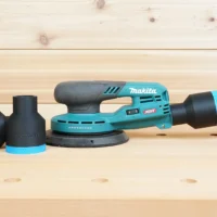 Black ToolCurve 1-7/8 inch hose adapter with blue ring installed on a Makita XGT sander dust port, spare adapter beside it