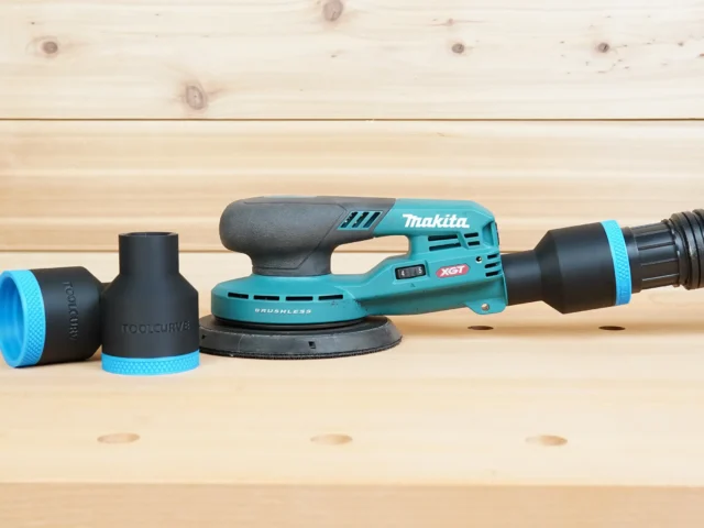 Black ToolCurve 1-7/8 inch hose adapter with blue ring installed on a Makita XGT sander dust port, spare adapter beside it