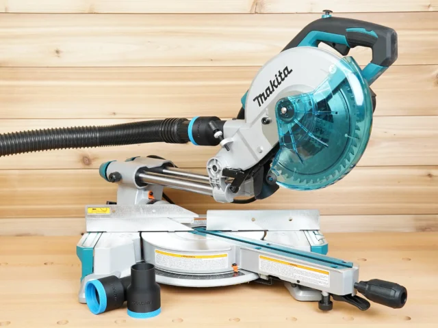 ToolCurve 1-7/8 inch hose adapter installed on a Makita LS miter saw dust port with hose attached, plus two spare adapters on the bench
