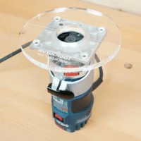 6-inch round clear acrylic base plate mounted on a Bosch Colt trim router, showing the flat routing surface and center spindle opening