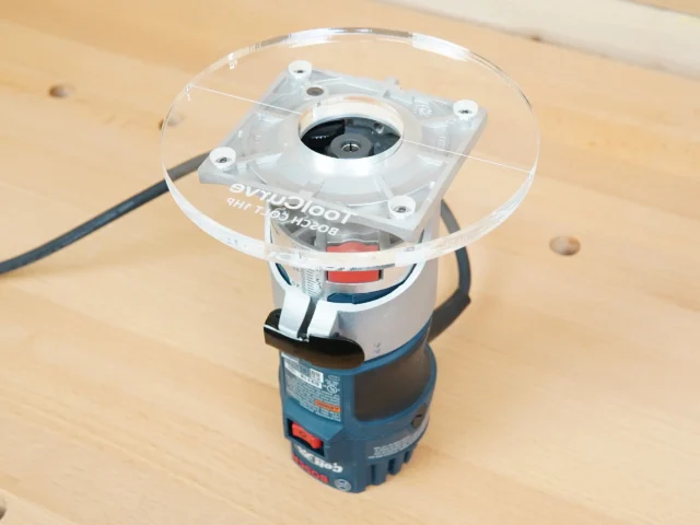 6-inch round clear acrylic base plate mounted on a Bosch Colt trim router, showing the flat routing surface and center spindle opening