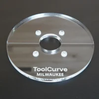 Clear acrylic router base plate with central spindle opening, four mounting holes, and metal reinforcement ring around center hole