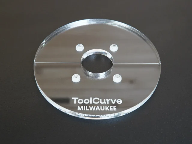 Clear acrylic router base plate with central spindle opening, four mounting holes, and metal reinforcement ring around center hole