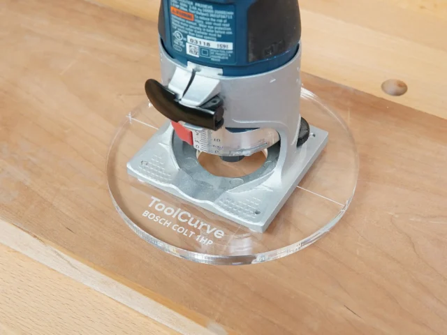 Clear acrylic router base plate mounted on Bosch Colt 1 HP trim router, showing 6-inch diameter and ruler marking on the base