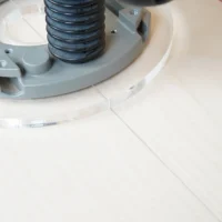 8-inch clear acrylic router base plate attached to Bosch 1617 router, showing threaded center post and mounting hardware on white wood surface