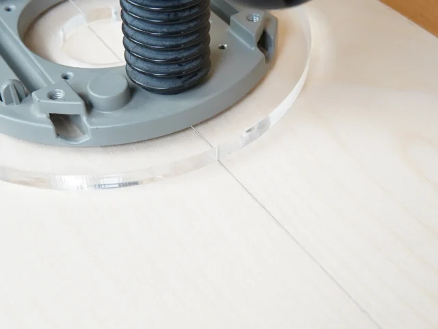 8-inch clear acrylic router base plate attached to Bosch 1617 router, showing threaded center post and mounting hardware on white wood surface