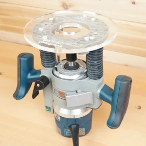 Clear 8-inch acrylic router base plate resting above a blue Bosch 1617 plunge router on a pine benchtop