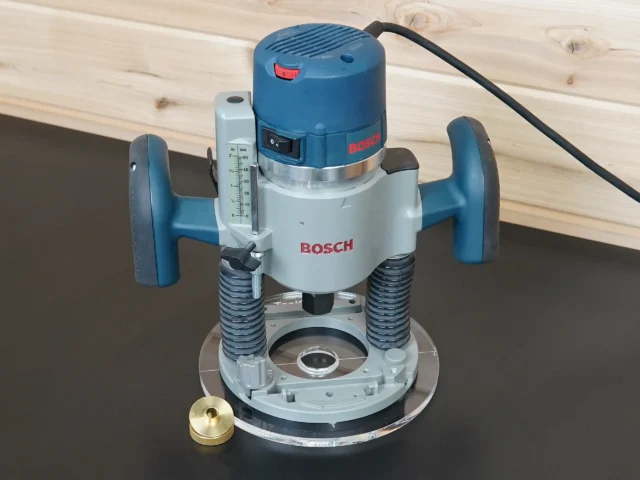 Bosch 1617 plunge router on a clear 8-inch round acrylic guide bushing base plate, brass bushing beside it