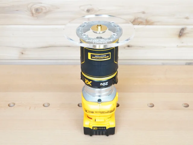 6-inch round clear acrylic router base plate attached to yellow DeWalt trim router, shown from above on wood workbench