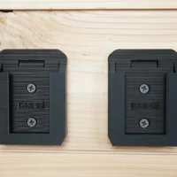 Two black plastic battery mounts for Kreg 18v batteries mounted on light wood, each with a central slot and two screw holes