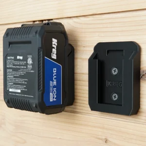 Two black Kreg 18v battery wall mounts screwed to a pine board, one holding a Kreg 20V 4Ah battery