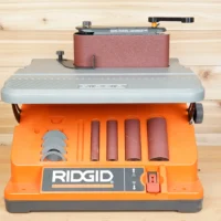 Ridgid oscillating edge sander with wrench-style tool positioned over front adjustment knob, showing sanding drums and belt below
